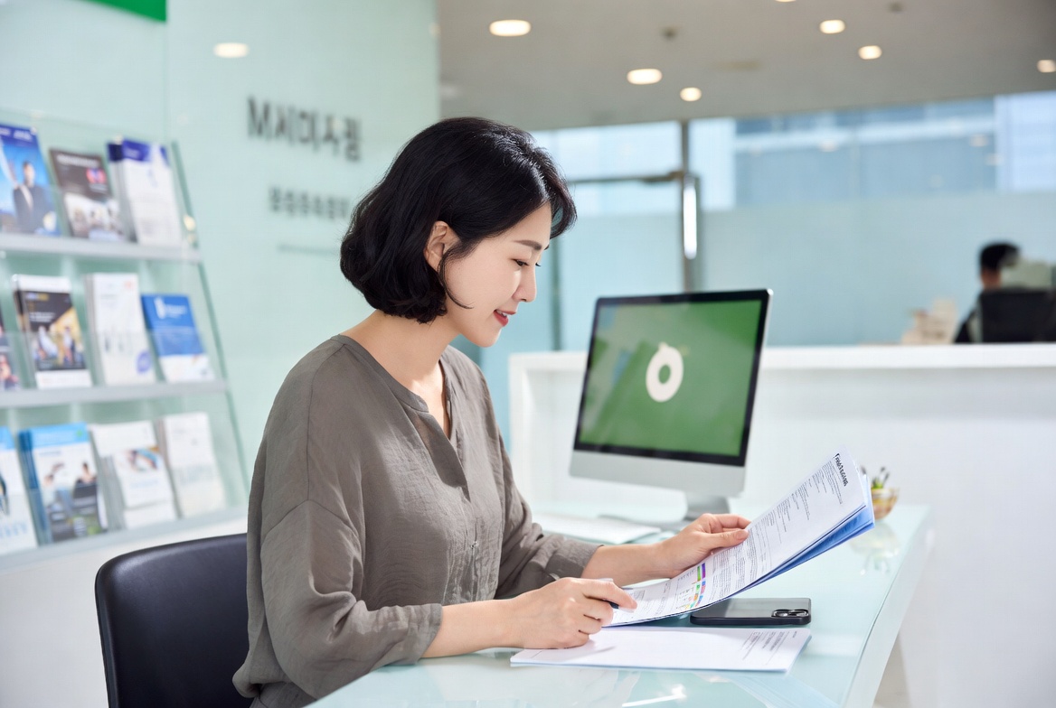 은행 창구에 앉아 스마트폰과 안내 책자를 비교하며 계좌 개설을 고민하는 모습