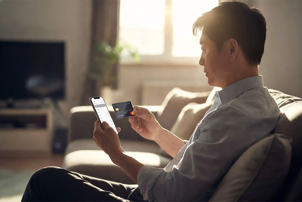거실 소파에 앉아 신용카드와 스마트폰으로 한도를 상향하는 40대 남성