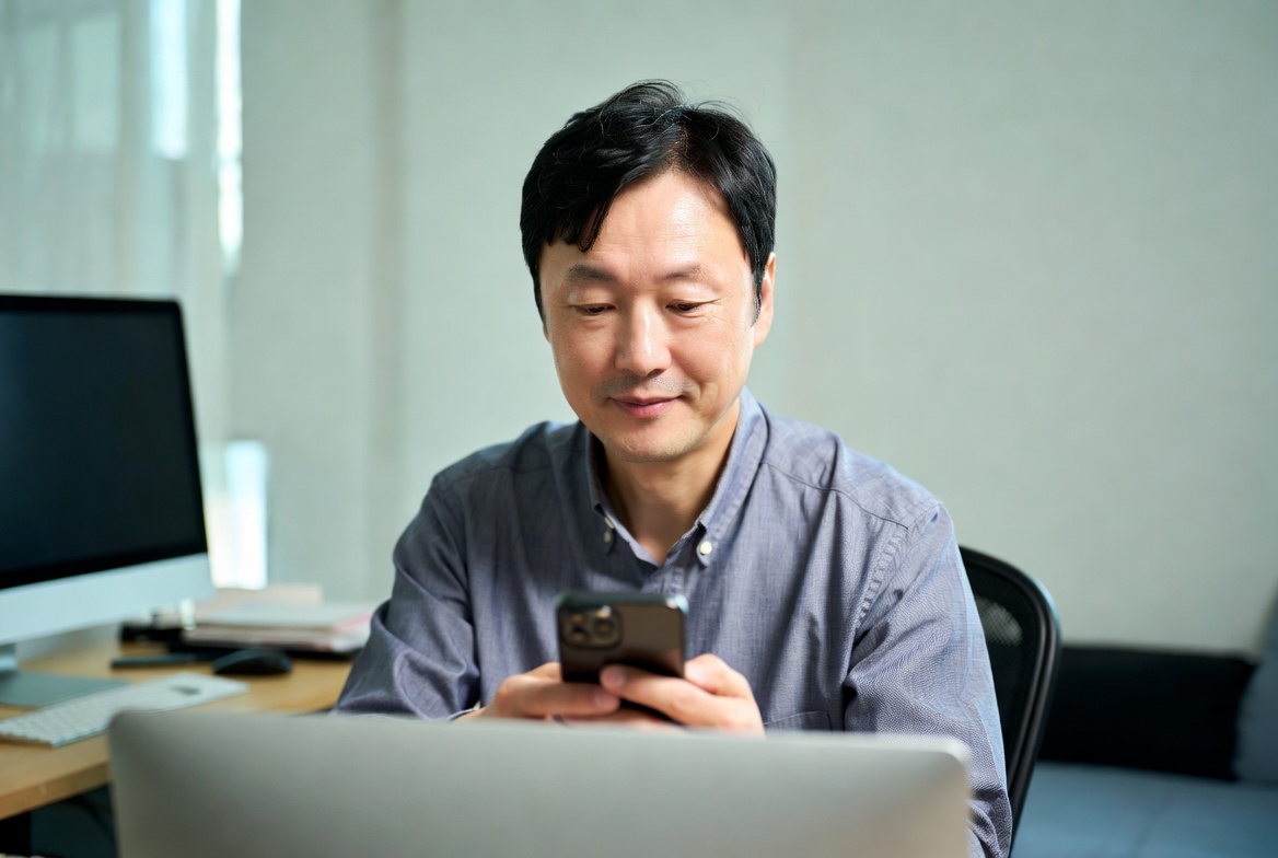 가정집 서재에서 중년 남성이 스마트폰으로 금융 앱을 확인하는 모습