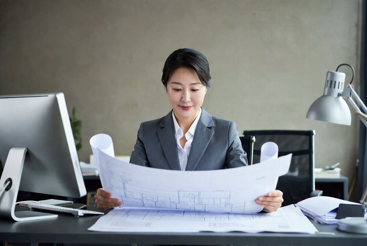 기업 오피스에서 재건축 관련 도면과 세무 신고 서류를 꼼꼼히 대조하는 모습