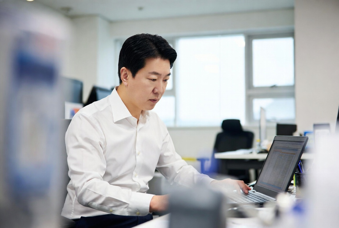 45~55세 한국 남성이 사무실 책상에 앉아 노트북으로 세법 규정을 심각하게 확인하는 모습