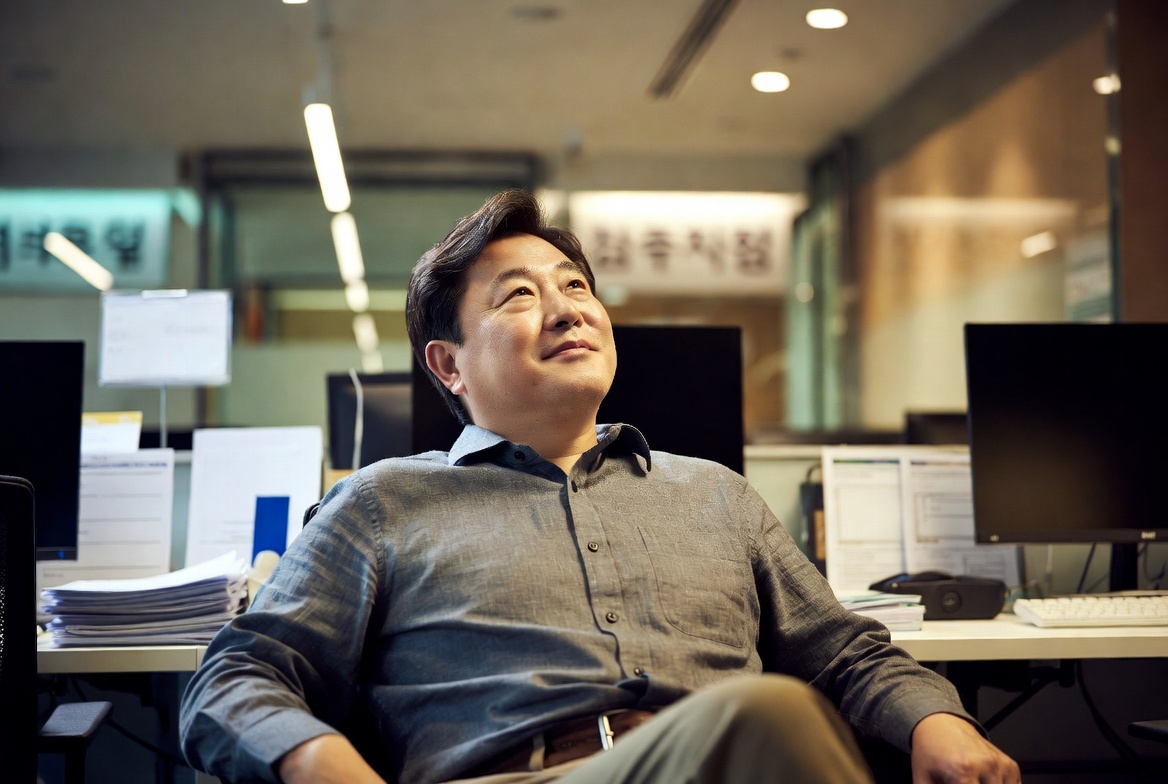45~55세 한국 남성이 기업 오피스에서 의자에 기대어 만족스러운 표정으로 전략을 구상하는 장면