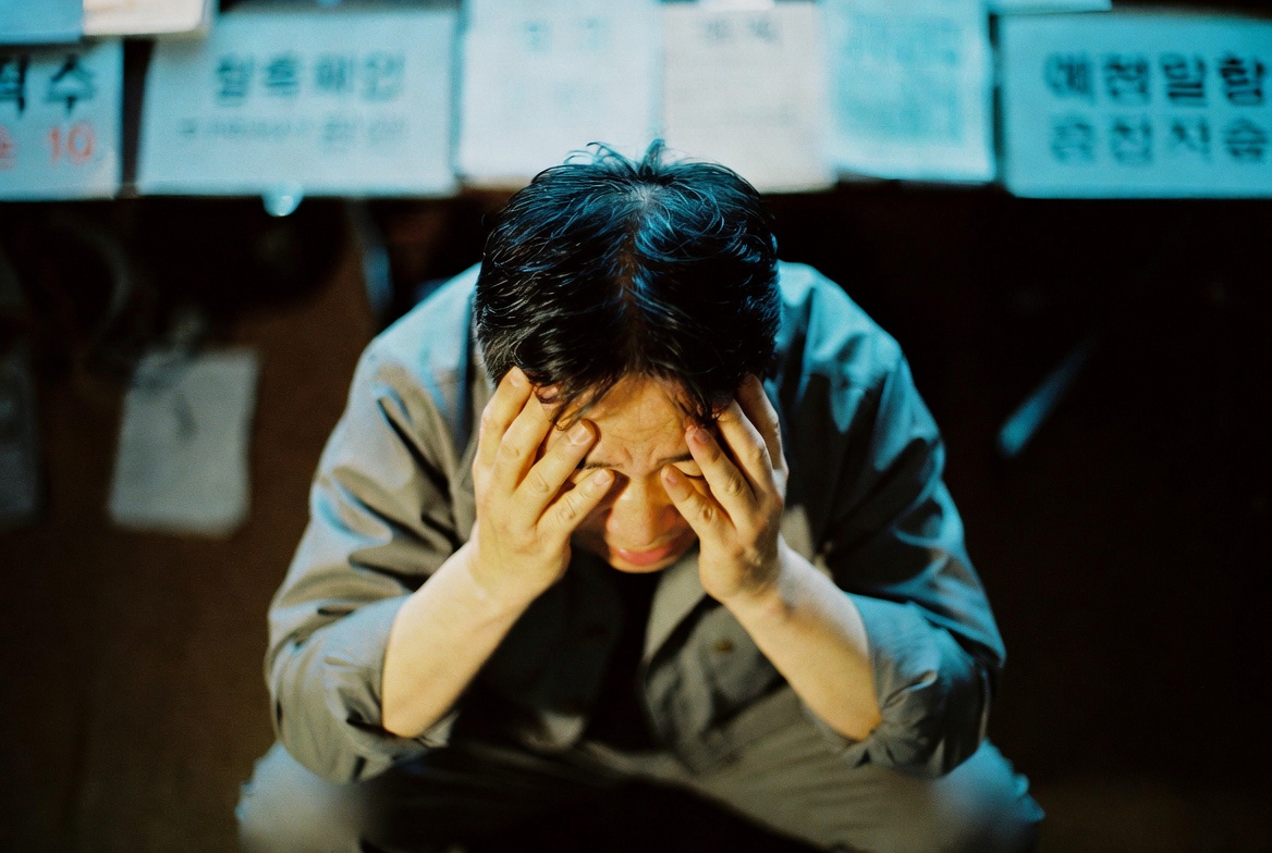 45~55세 한국 남성이 로우 앵글 구도에서 손으로 얼굴을 감싸고 고개를 숙인 채 세무조사 통지서를 보며 심각하게 긴장한 모습